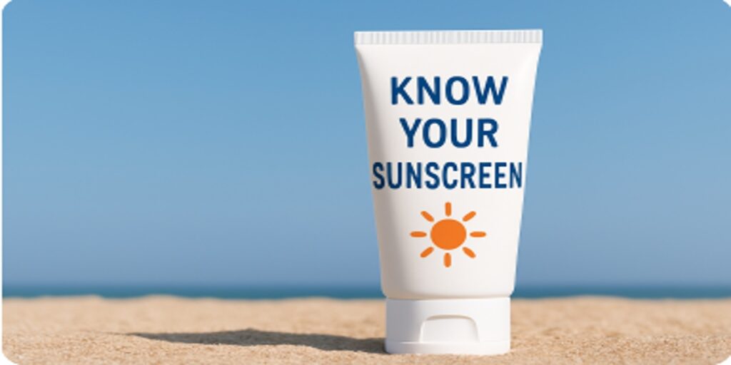 A white bottle of sunscreen standing on the sand with the words 'Know Your Sunscreen' printed on it, under a clear blue sky.